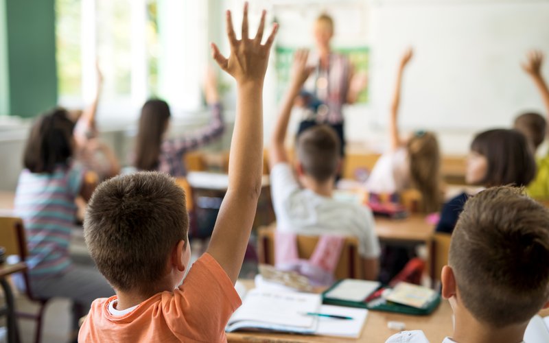 Kinder im Klassenraum, die sich melden.