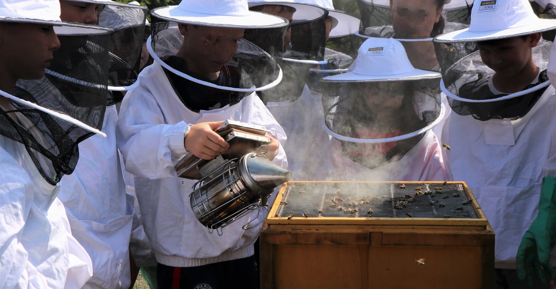 Kinder in Imkerkleidung vor einem Bienenkasten.